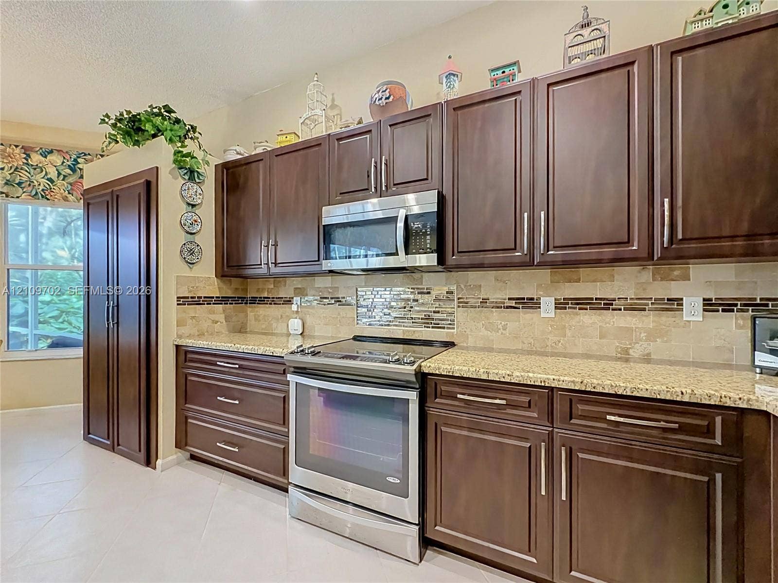 Kitchen featuring dark-toned cabinetry, stone-finish countertops, stainless steel appliances, and a decorative tile backsplash