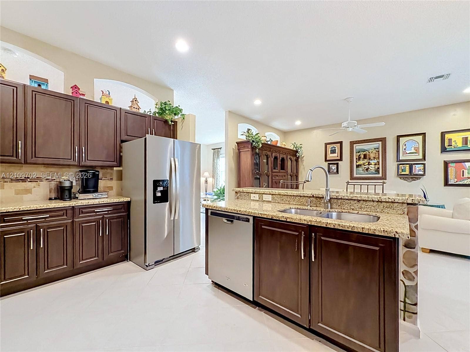 Kitchen featuring dark-finish cabinetry, stone-style countertops, stainless steel appliances, a dual-basin undermount sink, and tile flooring