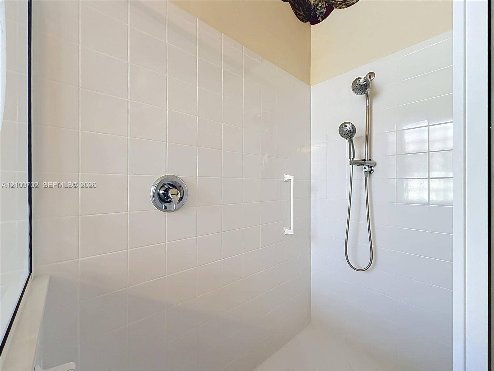 Shower enclosure featuring white square wall tiling, a chrome single-handle pressure balance valve, a dual-head shower system with a handheld attachment, and a white grab bar