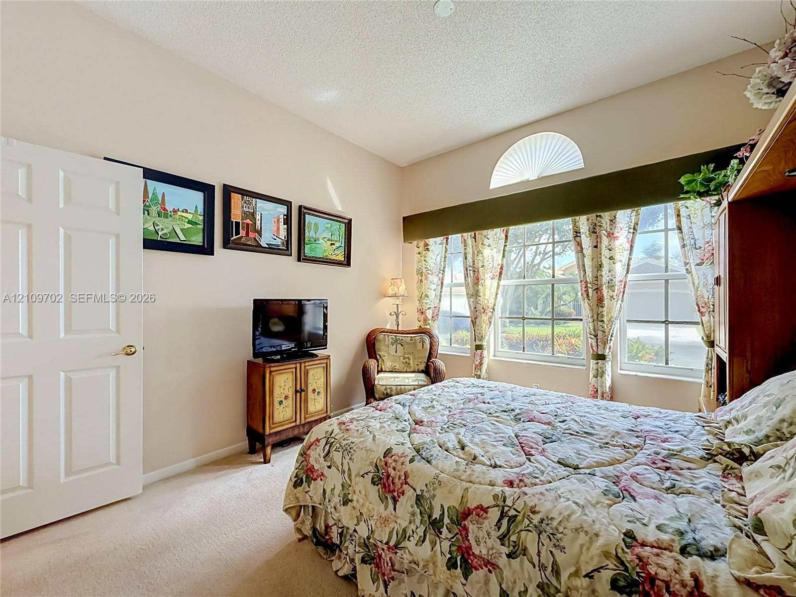 Neutral-toned room featuring high ceilings, carpeting, expansive windows with a decorative arched transom, and a six-panel interior door