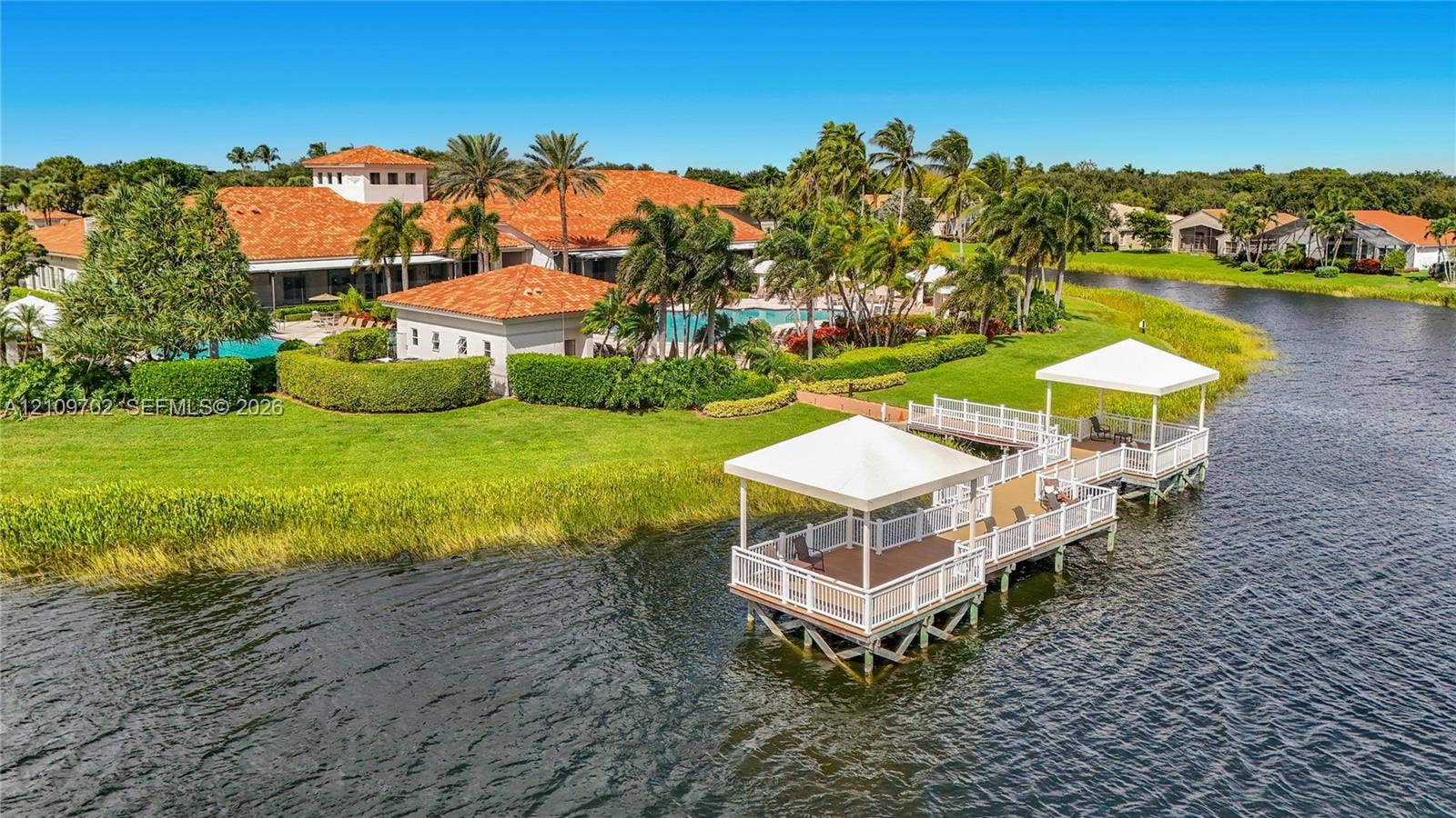 Waterfront Clubhouse featuring twin covered docks, a terracotta tile roof, and manicured landscaping