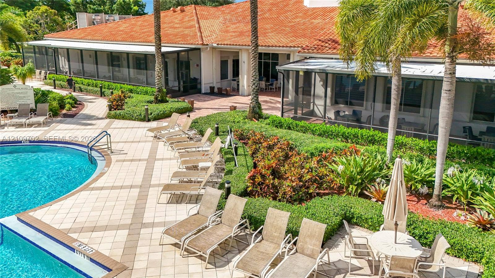 Tile-roofed exterior featuring a swimming pool, expansive paver deck, and manicured landscaping with mature palms