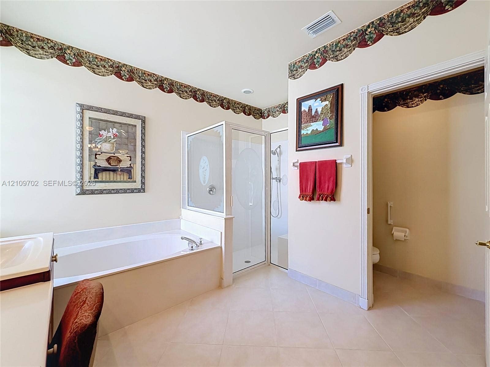 Bathroom featuring a built-in soaking tub with a tiled surround, a separate glass-enclosed shower, a double vanity, and tile flooring