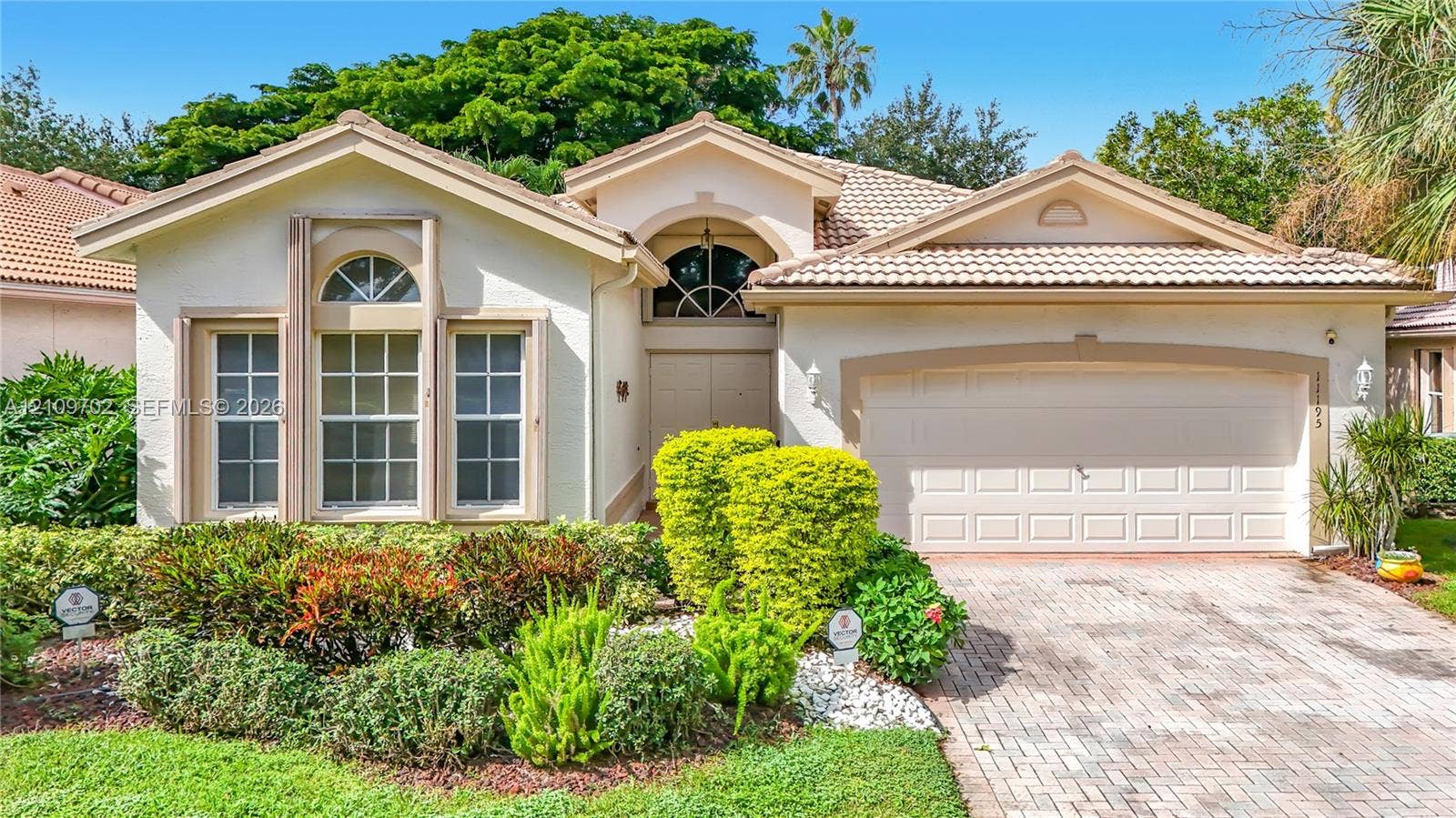 Stucco exterior featuring arched windows, tile roof, and a paved stone driveway