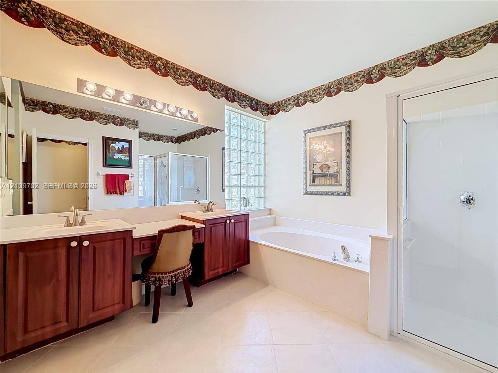 Bathroom featuring dual-sink vanity with wood-finish cabinetry, glass block window, deep soaking tub, and enclosed glass shower