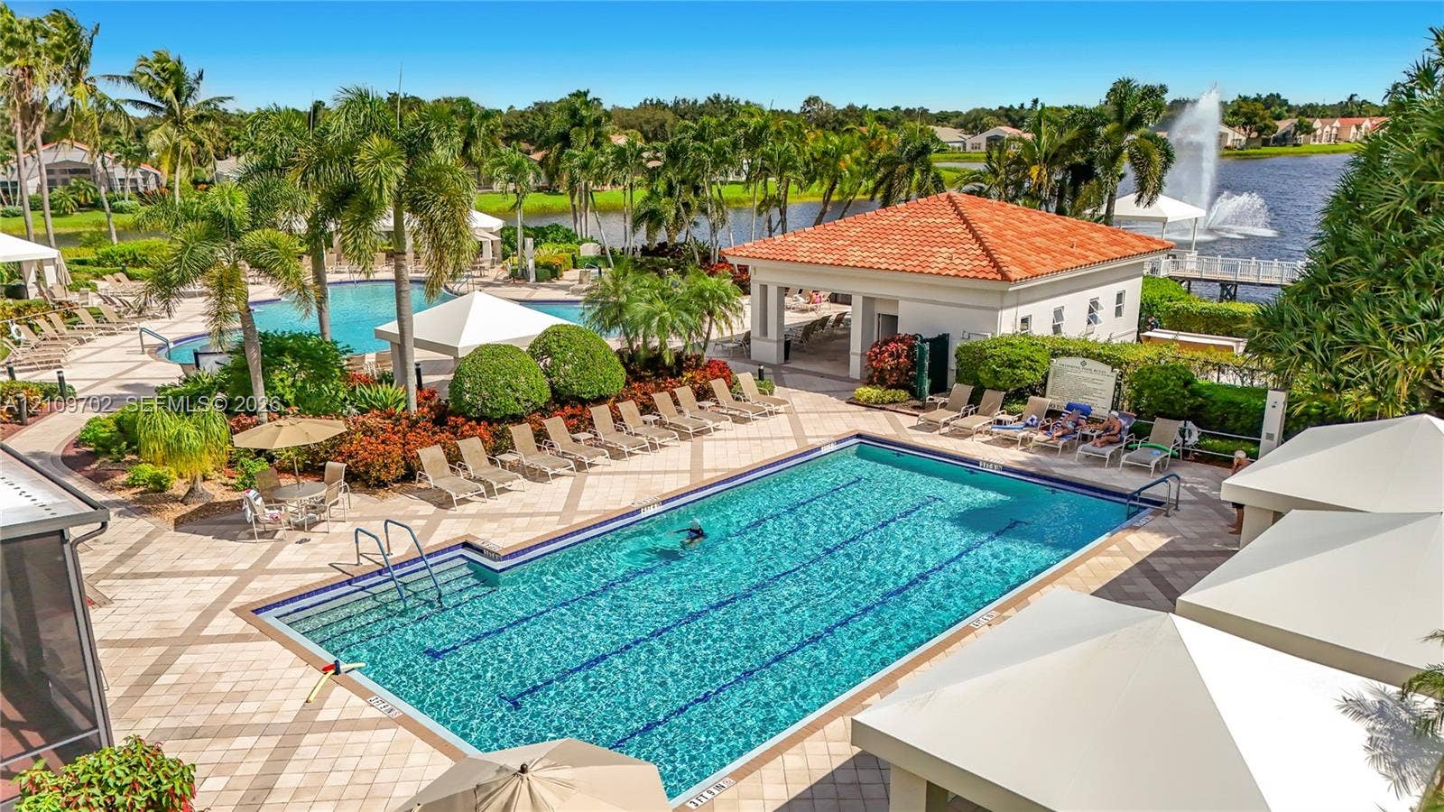 Community swimming pool featuring lane markings, paver deck, covered pavilion with tile roof, and waterfront scenery