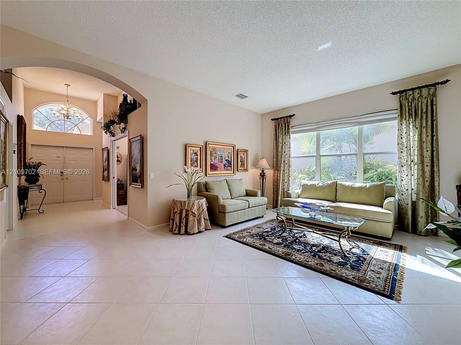 Spacious interior featuring high ceilings, light-toned ceramic tile flooring, a prominent arched architectural opening, and a large multi-pane window with a half-moon transom light