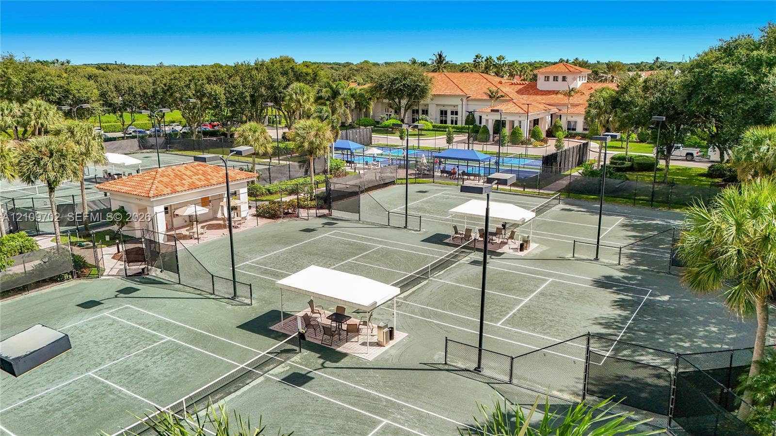 Multiple hard-surface tennis courts featuring perimeter fencing, integrated shade structures, and manicured landscaping