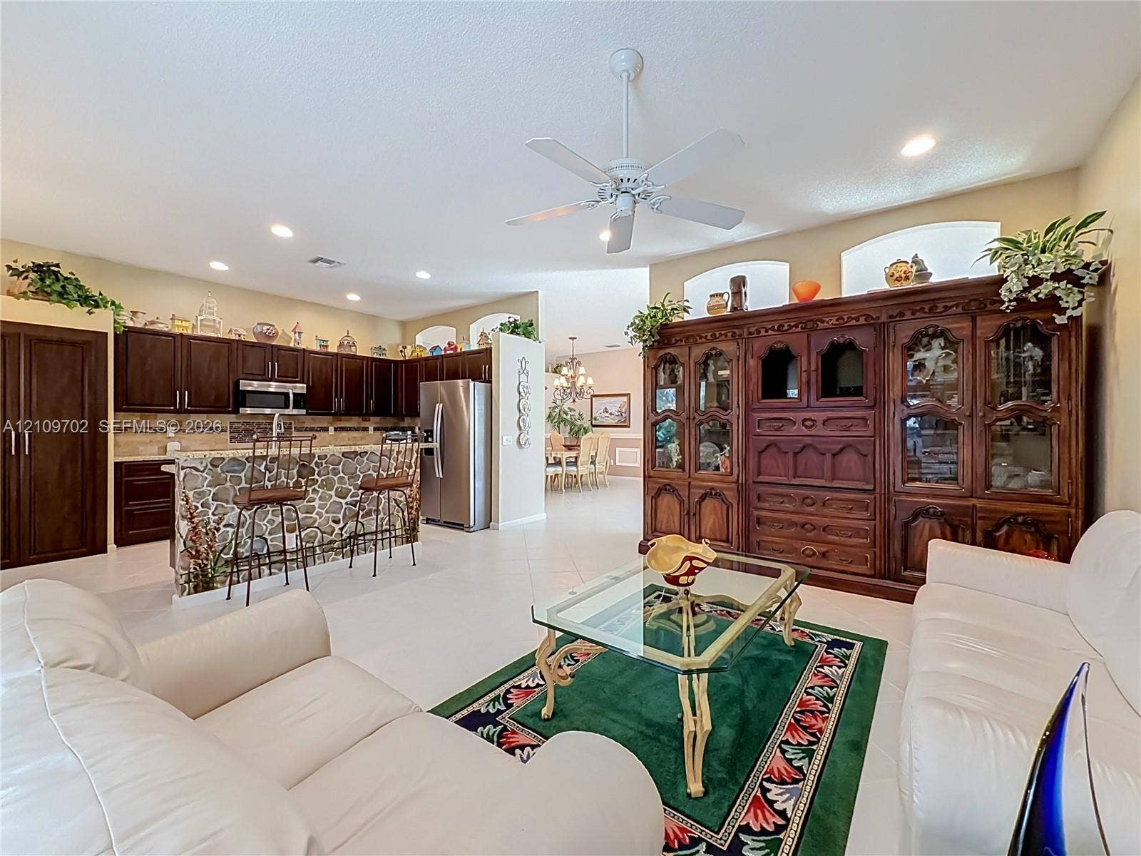 Open-concept area featuring tile flooring, recessed lighting, ceiling fan, stone-veneer kitchen island, and custom built-in cabinetry with glass display shelving