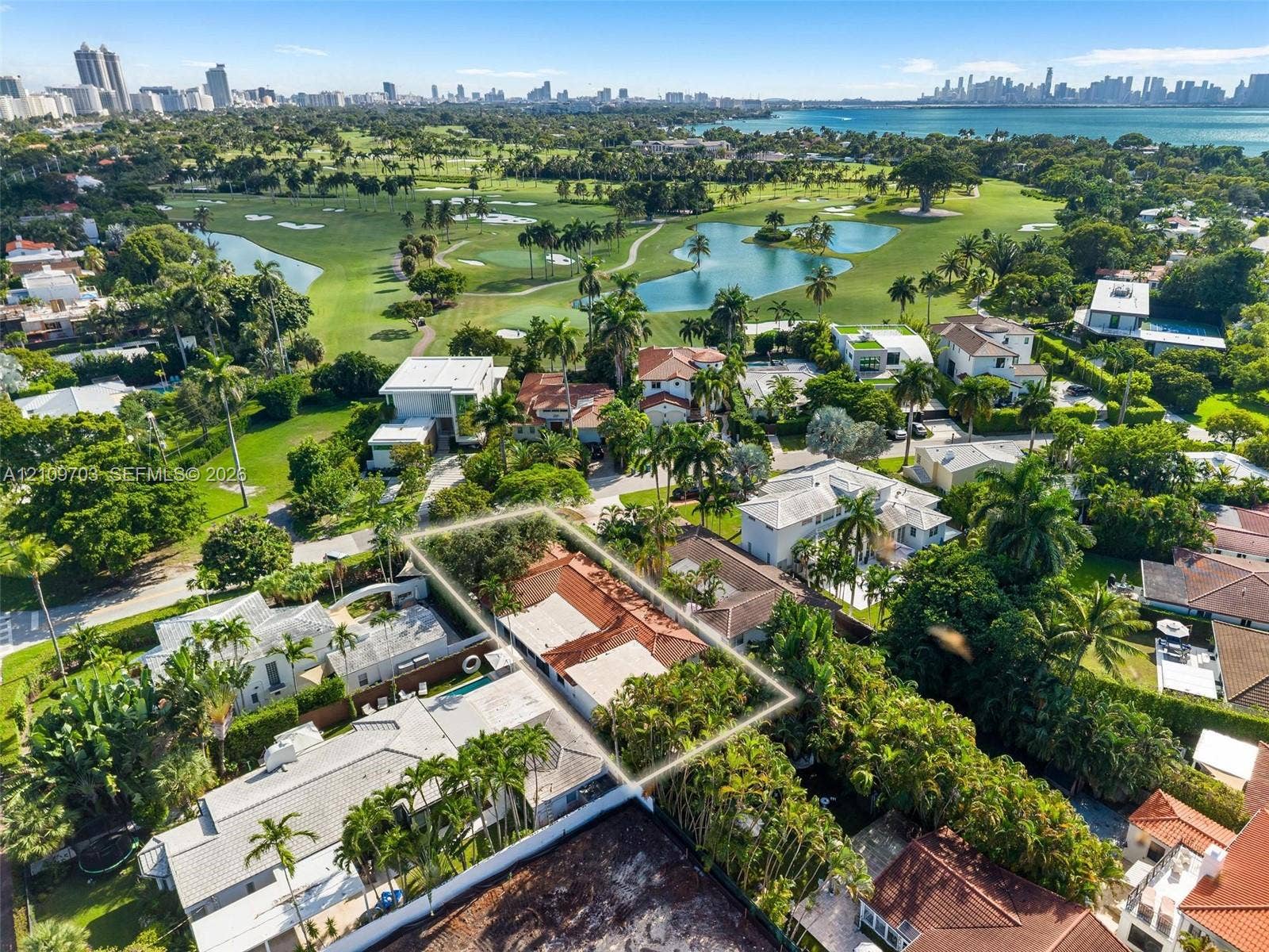 421 W 62nd Street, Miami Beach, FL 33140 Aerial perspective highlighting a property with a clay tile roof, mature perimeter landscaping, and proximity to a golf course, water bodies, and coastal city skyline
