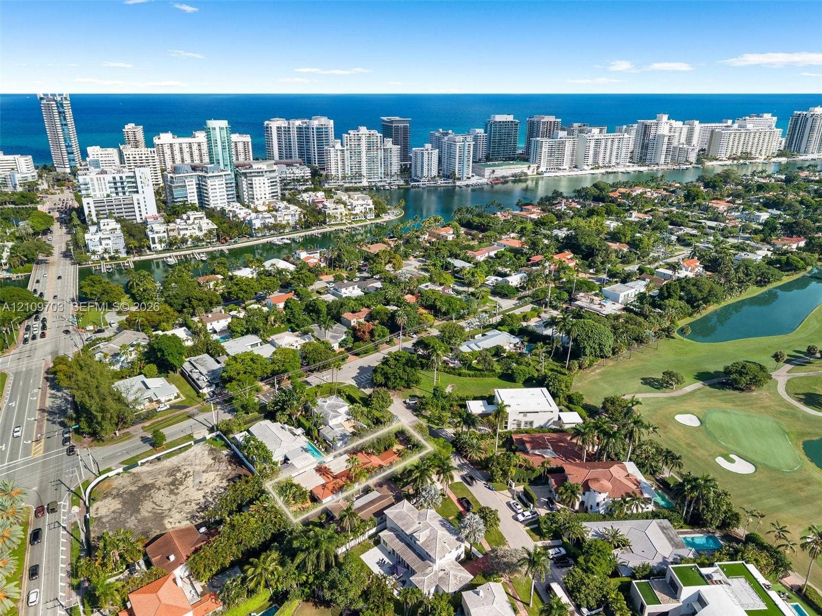 421 W 62nd Street, Miami Beach, FL 33140 Aerial perspective featuring a single-story residence with a clay tile roof, a swimming pool, and mature palm trees, positioned in a coastal setting with proximity to a golf course and urban skyline