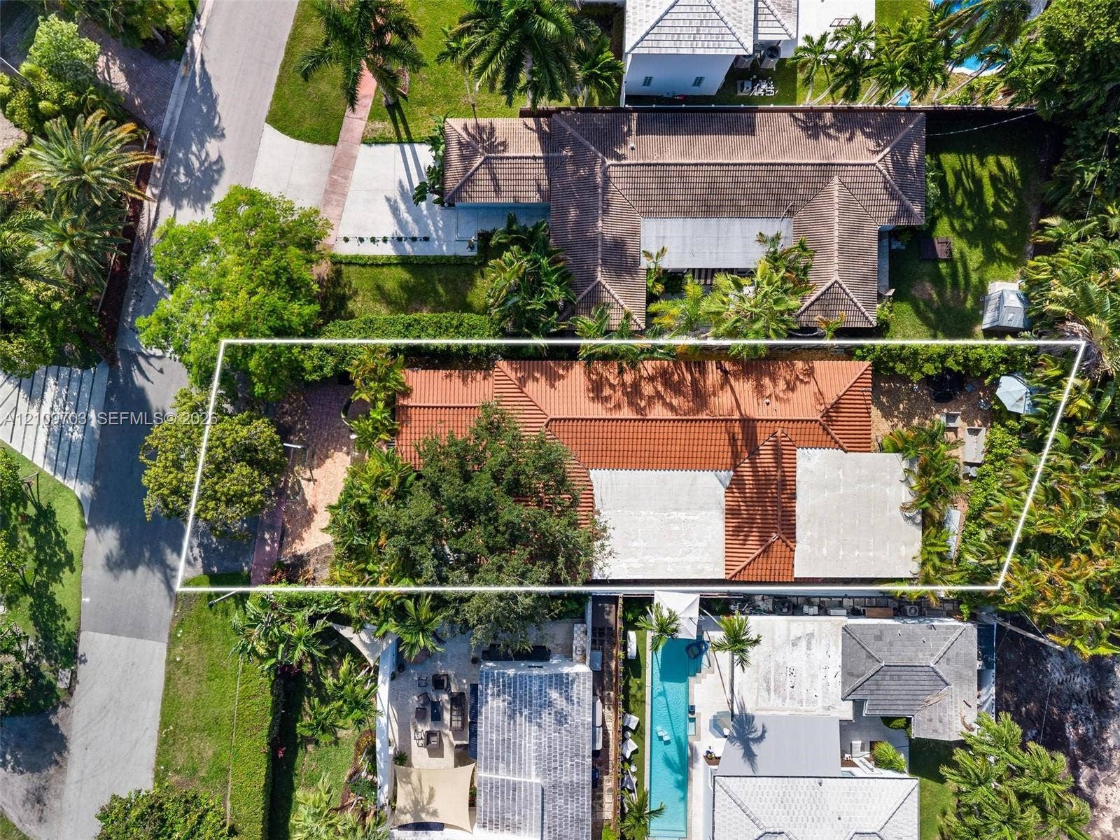 421 W 62nd Street, Miami Beach, FL 33140 Aerial perspective featuring a terracotta-tiled roof, paved driveway, dense perimeter landscaping, and mature canopy trees on a corner lot