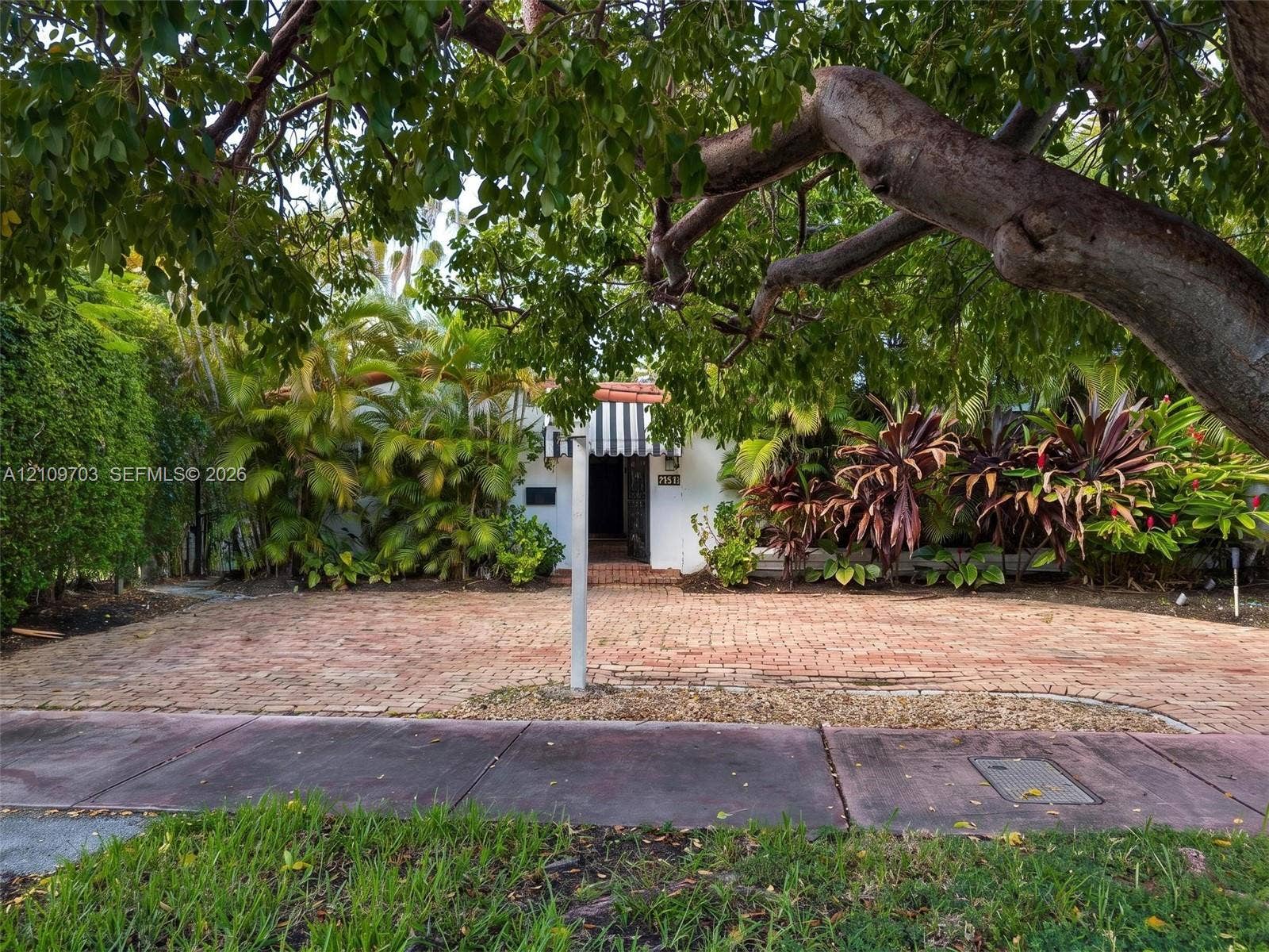 421 W 62nd Street, Miami Beach, FL 33140 Brick-paved driveway, striped window awning, mature canopy trees, and established perimeter landscaping