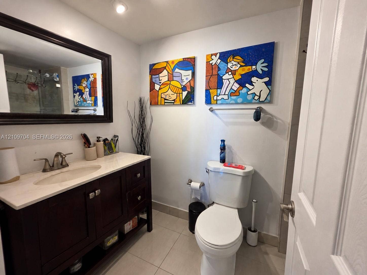 6770 Indian Creek Drive, #14C, Miami Beach, FL 33141 Bathroom featuring a dark-finish wood vanity, integrated sink with a metallic faucet, stone-composite countertop, large framed wall mirror, and neutral tile flooring