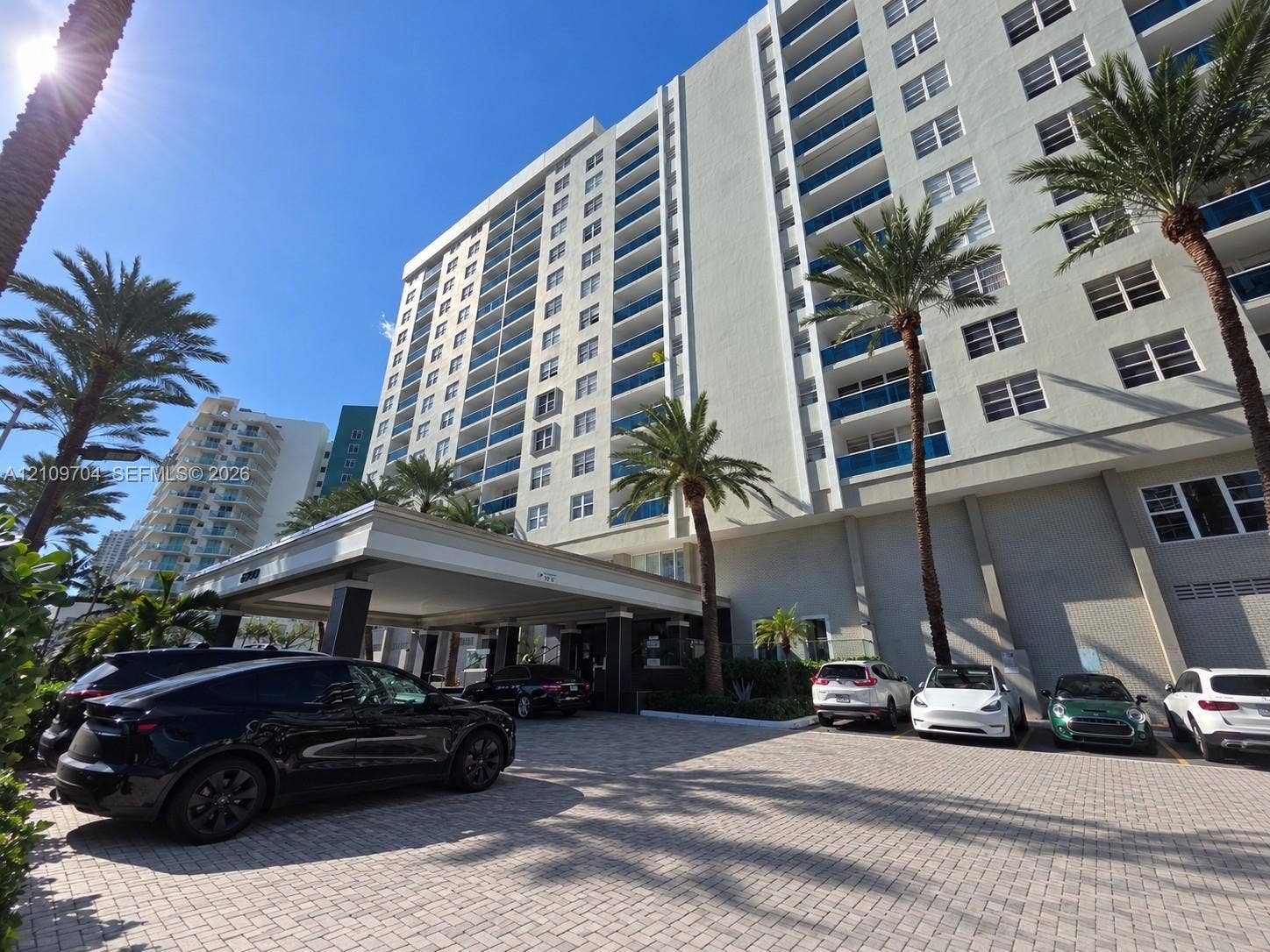 6770 Indian Creek Drive, #14C, Miami Beach, FL 33141 High-rise residential building featuring a paved motor court, covered porte-cochre, multi-story private balconies, and mature palm tree landscaping