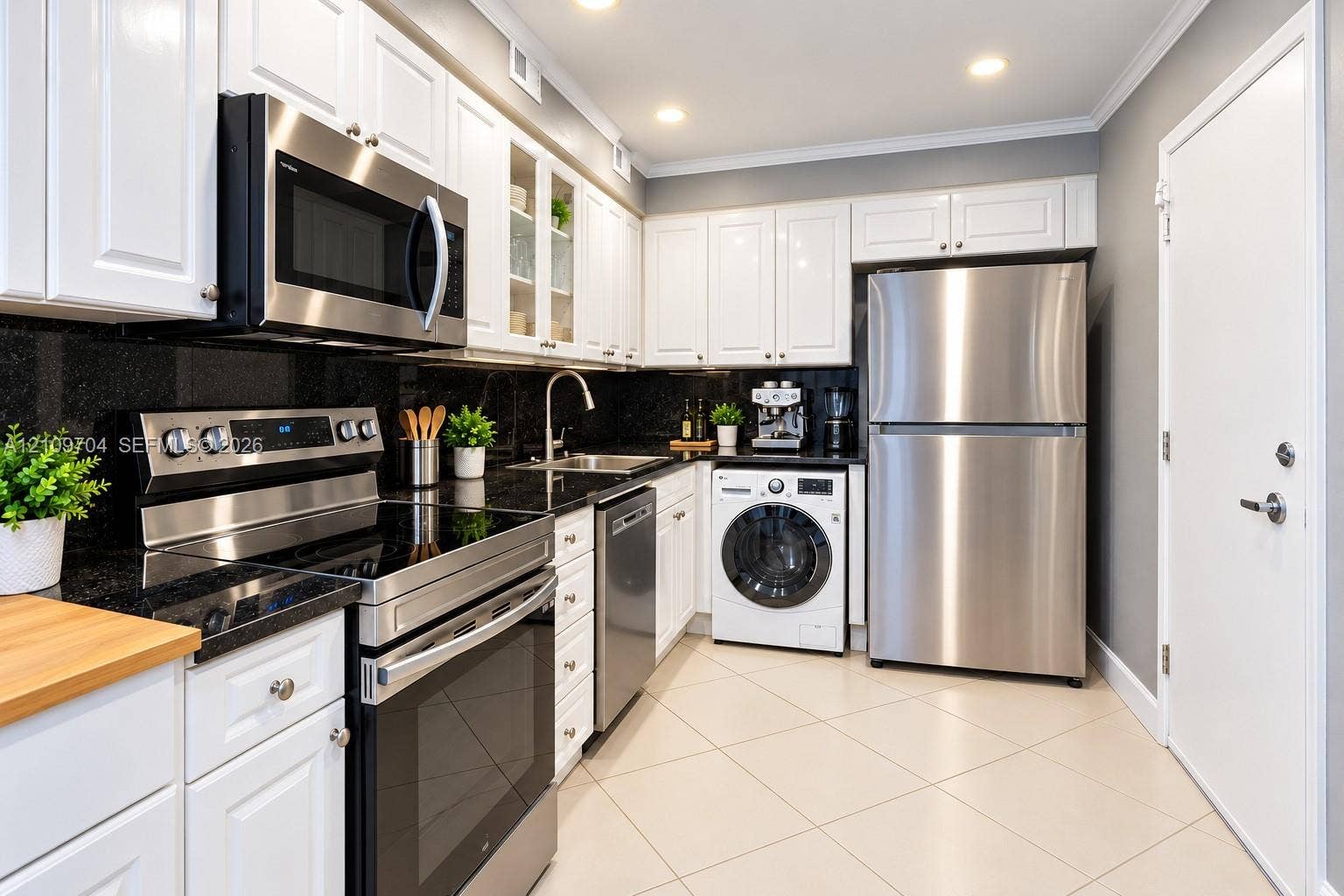 6770 Indian Creek Drive, #14C, Miami Beach, FL 33141 Kitchen featuring white shaker-style cabinetry, dark stone countertops, stainless steel appliances, integrated laundry, and light-toned tile flooring