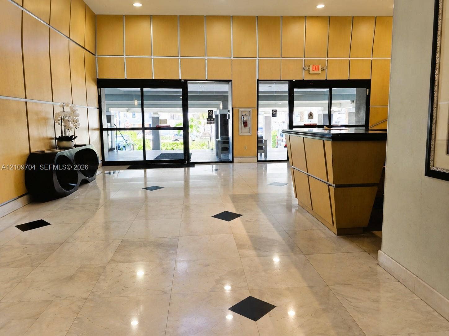 6770 Indian Creek Drive, #14C, Miami Beach, FL 33141 Lobby featuring polished tile flooring with inlaid stone accents, wood-paneled walls, built-in reception desk, and floor-to-ceiling glass entry doors with aluminum framing