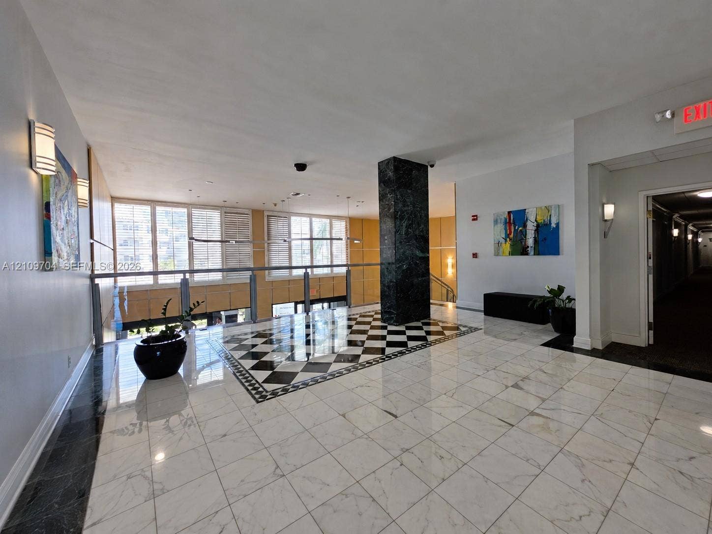 6770 Indian Creek Drive, #14C, Miami Beach, FL 33141 Lobby entrance featuring stone tile flooring with a checkered inset, a central dark stone-clad pillar, and multi-pane windows with integrated shutters