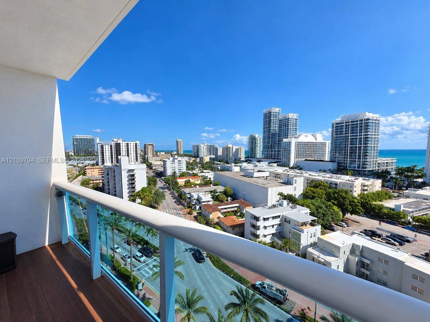 6770 Indian Creek Drive, #14C, Miami Beach, FL 33141 Covered balcony featuring wood-finish flooring and a glass panel railing with a metal top rail, offering an expansive cityscape and ocean horizon