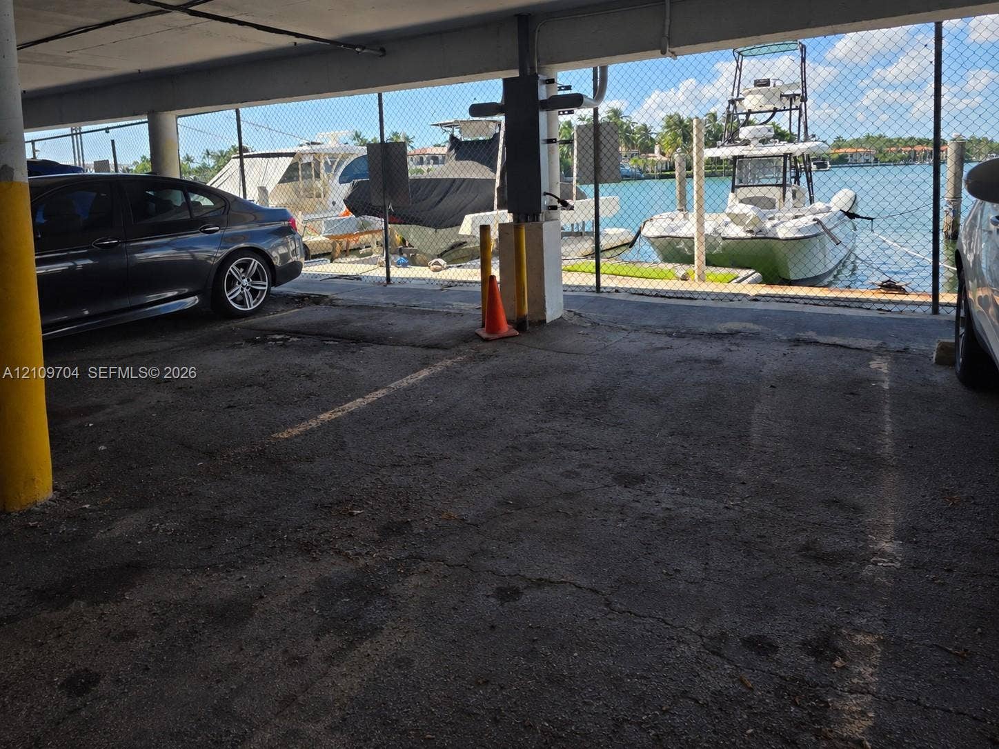 6770 Indian Creek Drive, #14C, Miami Beach, FL 33141 Covered parking space featuring asphalt paving, concrete support pillars, and direct proximity to a canal-side dock