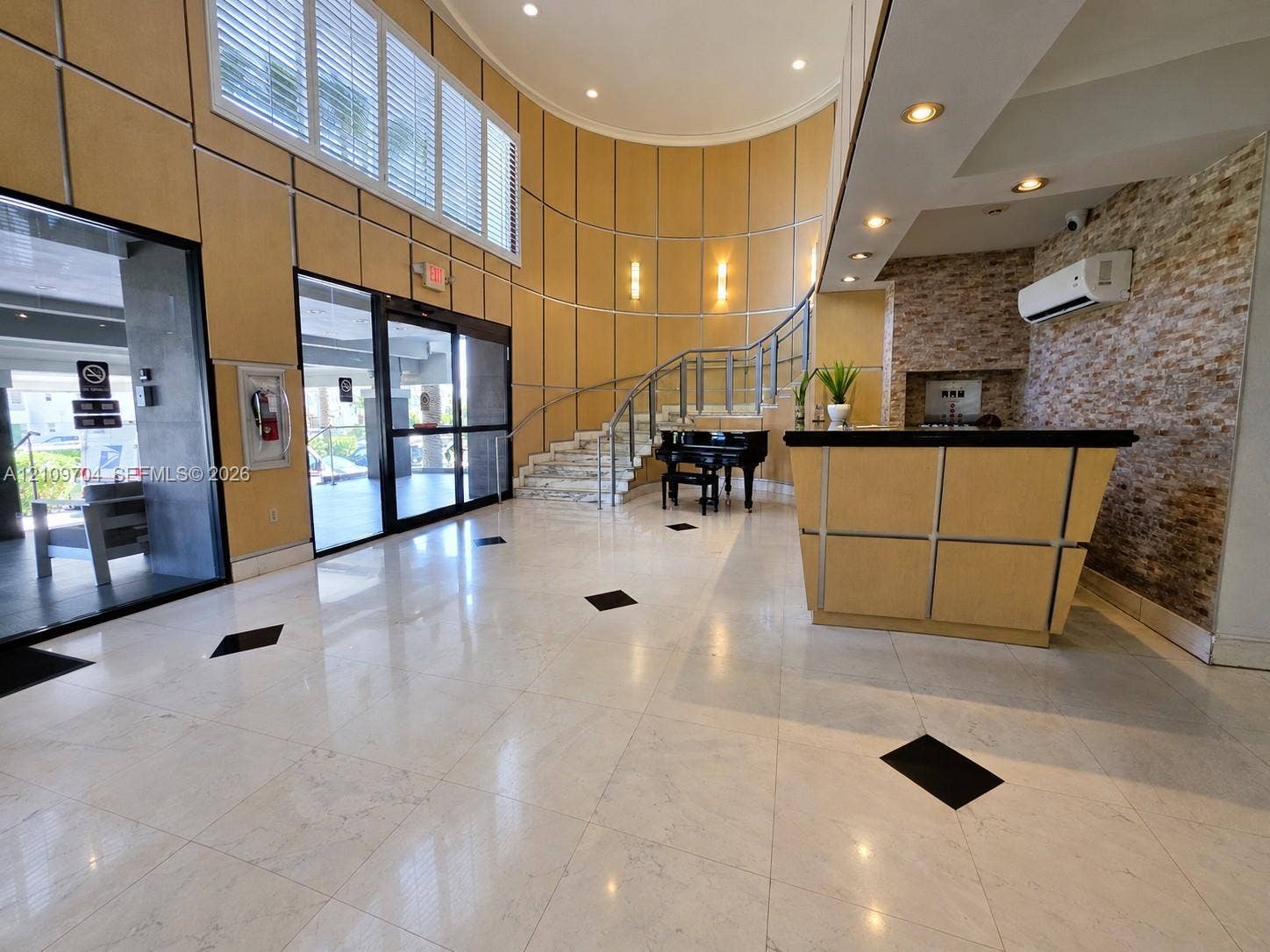 6770 Indian Creek Drive, #14C, Miami Beach, FL 33141 Polished tile flooring with geometric inlays, curved wall paneling, stone veneer accent wall, glass and metal staircase railing, and recessed ceiling lighting