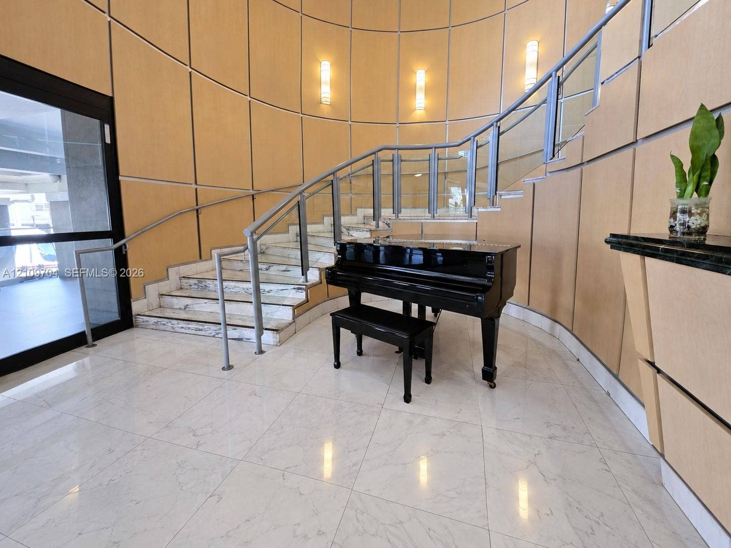 6770 Indian Creek Drive, #14C, Miami Beach, FL 33141 Curved staircase featuring stone treads, glass railings with metal handrails, polished tile flooring, and paneled wall finishes with integrated wall-mounted lighting