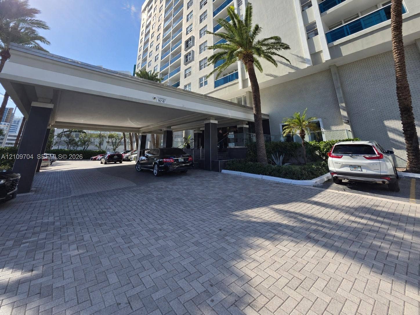6770 Indian Creek Drive, #14C, Miami Beach, FL 33141 High-rise exterior featuring a paved porte-cochre, covered drop-off area, multi-story facade with glass railings, and mature palm trees
