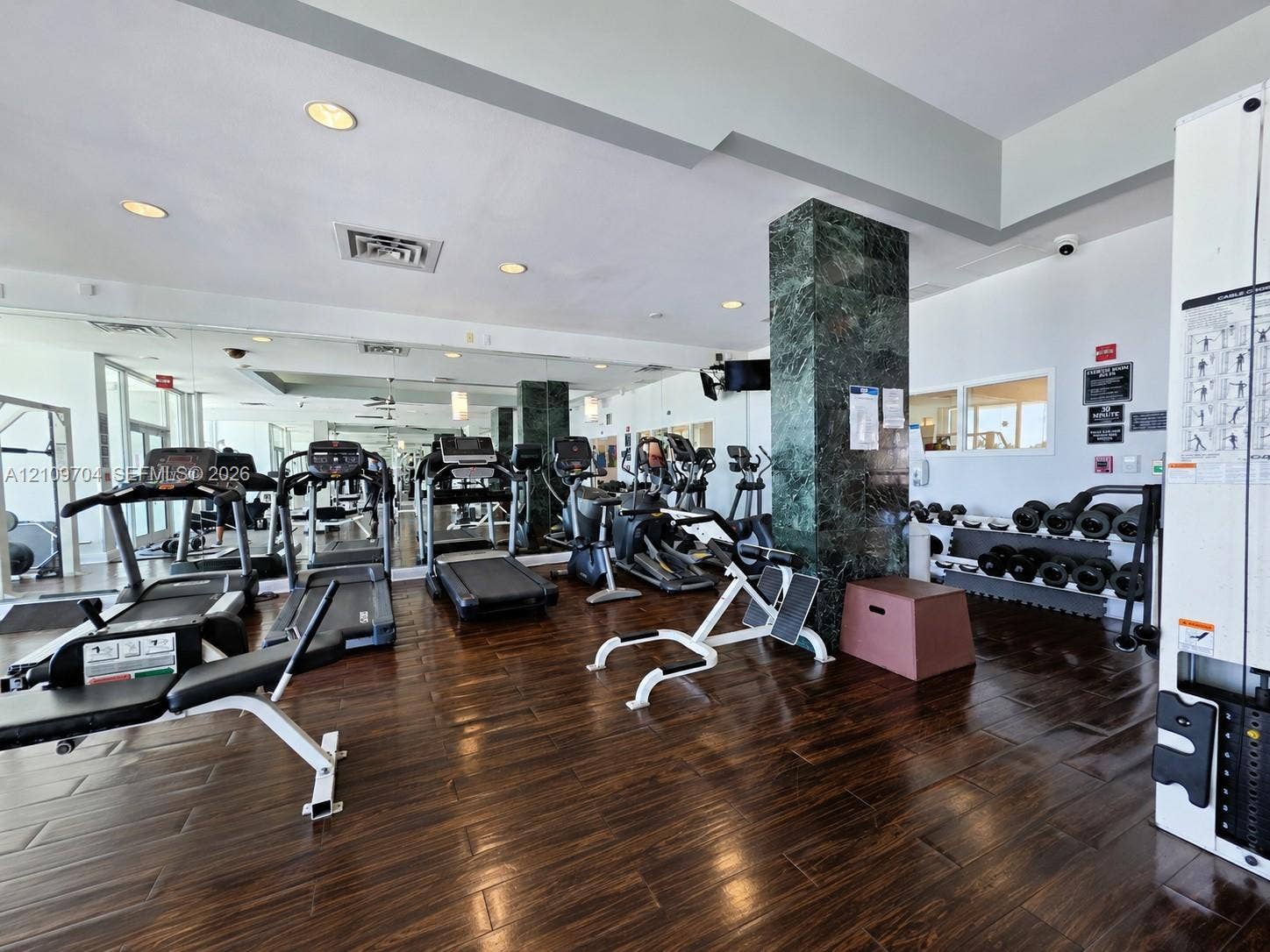 6770 Indian Creek Drive, #14C, Miami Beach, FL 33141 Fitness center featuring wood-finish flooring, floor-to-ceiling mirrored walls, and a decorative stone-clad structural column