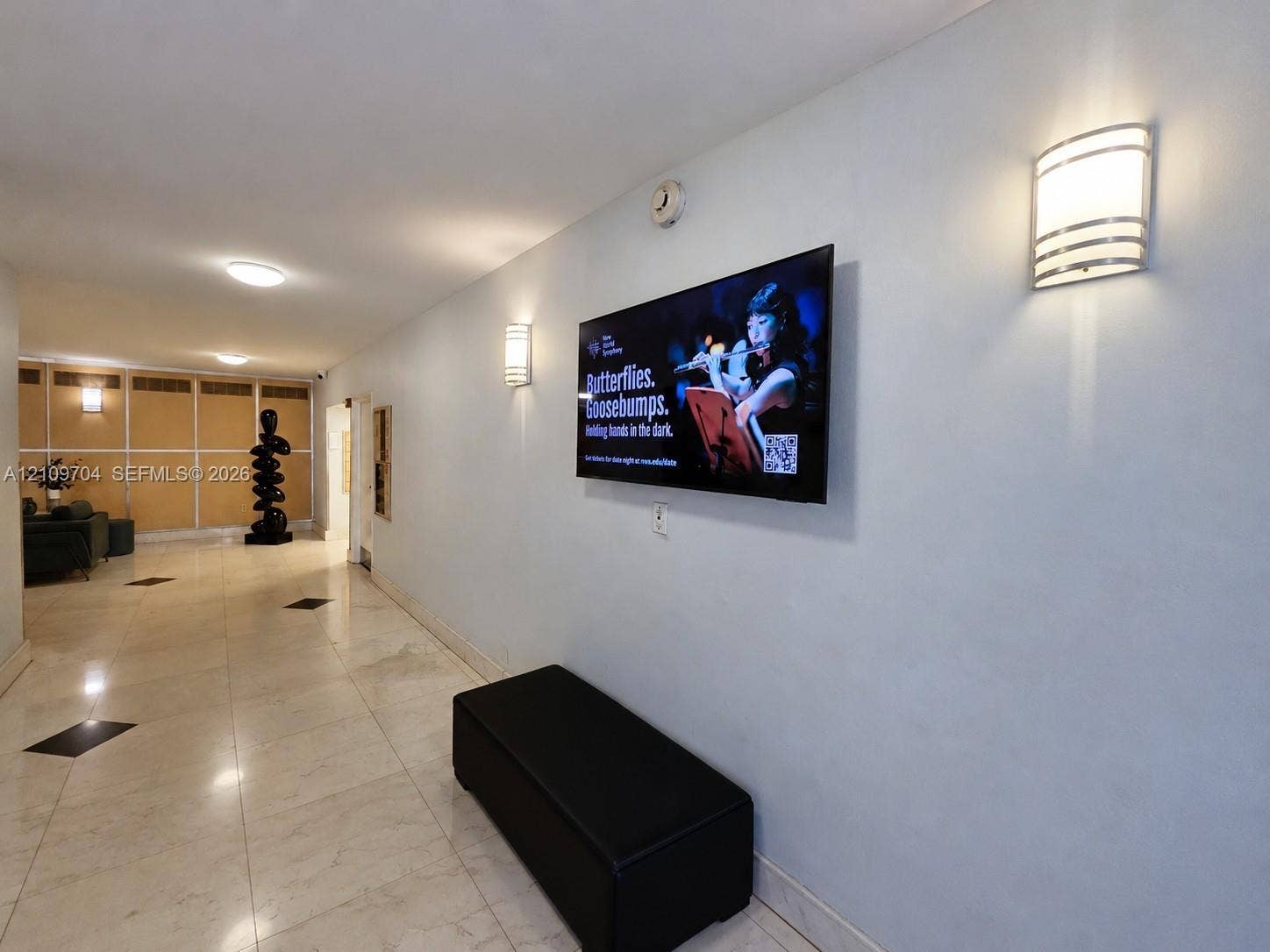 6770 Indian Creek Drive, #14C, Miami Beach, FL 33141 Neutral-toned corridor featuring polished stone flooring with inlaid geometric accents, recessed ceiling lighting, and wall-mounted metal sconces