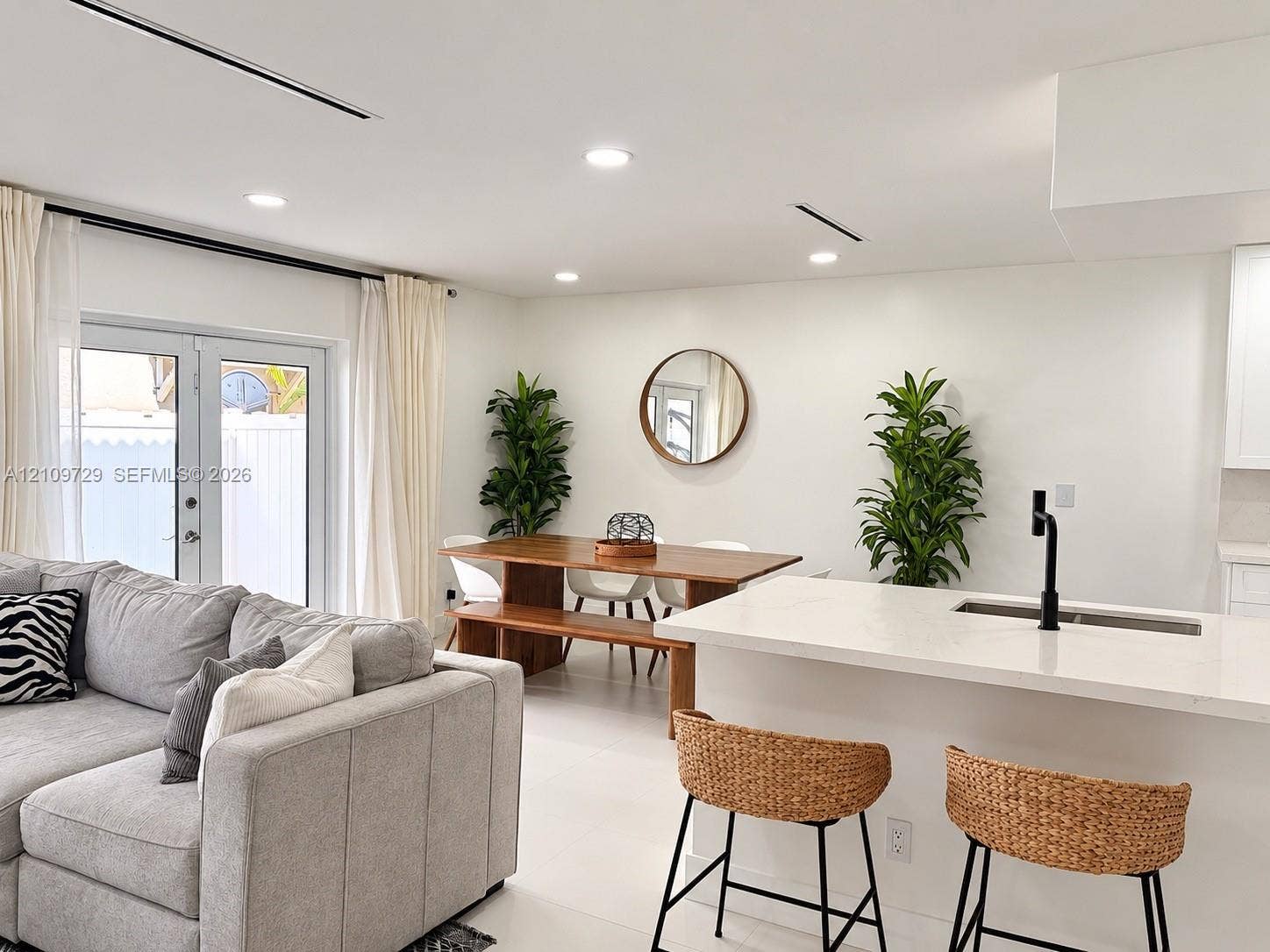 12665 SW 54th Court, Miramar, FL 33027 Open-concept living space featuring a central kitchen island with a light-toned countertop, matte black faucet, recessed ceiling lighting, and glass-paneled double doors