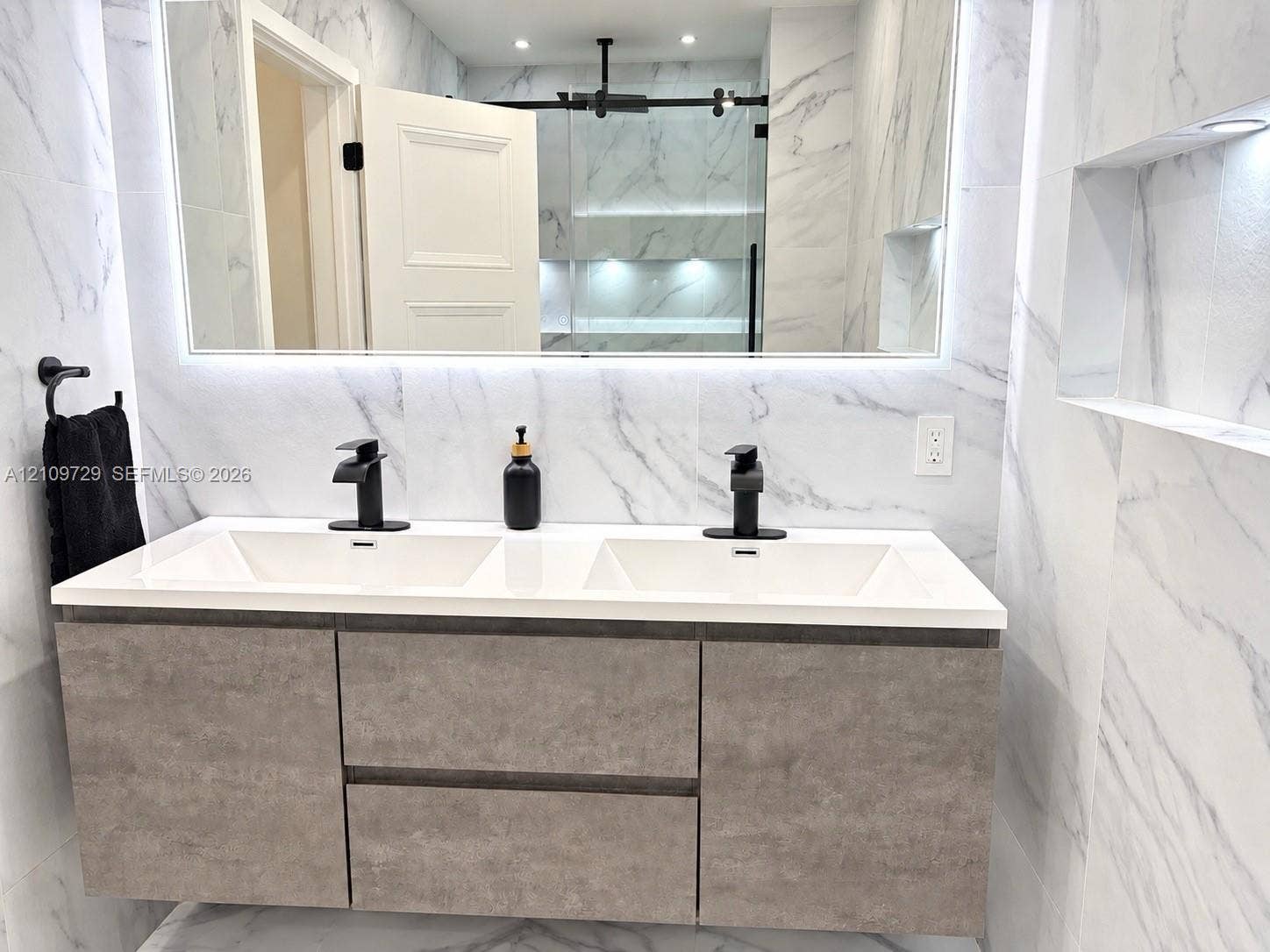 12665 SW 54th Court, Miramar, FL 33027 Floating double vanity with a composite countertop, dual matte black faucets, integrated LED-backlit mirror, and full-height wall tiling with recessed shelving
