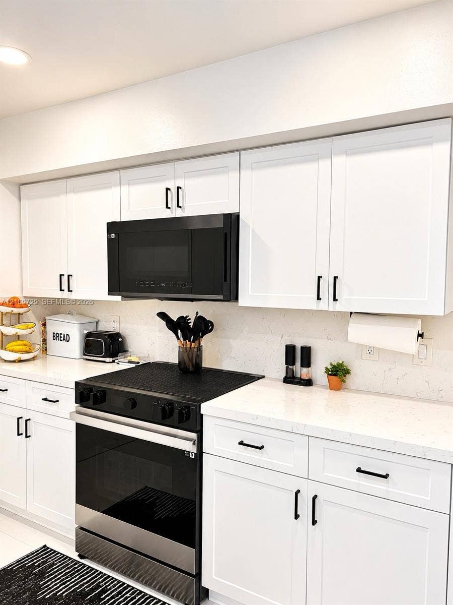 12665 SW 54th Court, Miramar, FL 33027 Kitchen featuring white shaker-style cabinetry, solid-surface countertops, a neutral stone-patterned backsplash, and matte black hardware