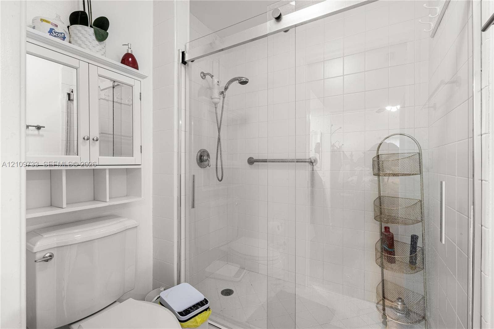 Walk-in shower with sliding glass door, white wall tiling, chrome shower fixtures, and built-in medicine cabinet with integrated shelving