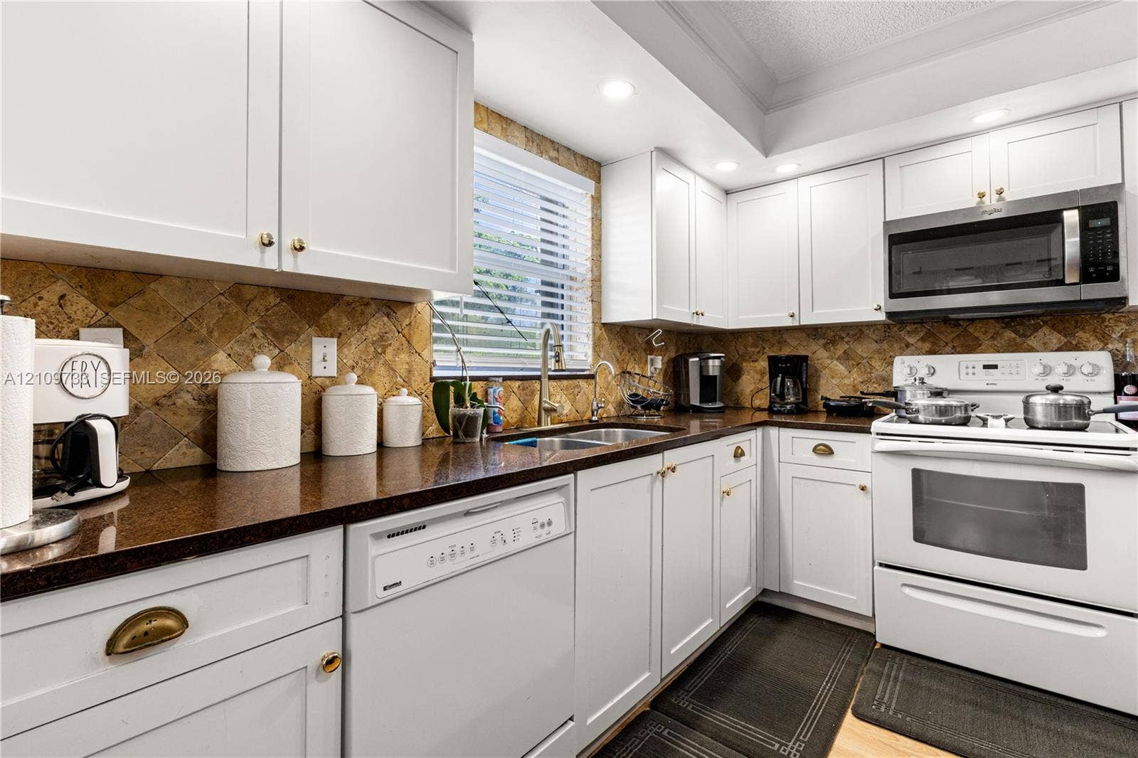 Kitchen featuring white cabinetry, stone-finish countertops, diagonal-set stone backsplash, recessed lighting, and stainless steel microwave