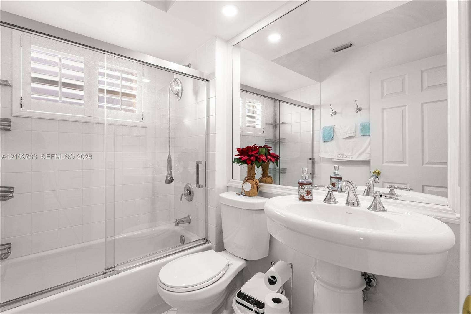 Bathroom featuring a shower-tub combination with a sliding glass door, white wall tiling, a pedestal sink with polished chrome fixtures, and a large-format mirror