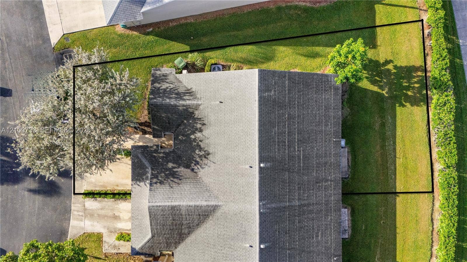 Aerial perspective highlighting a lot boundary, expansive lawn area, mature trees, and shingled roofline
