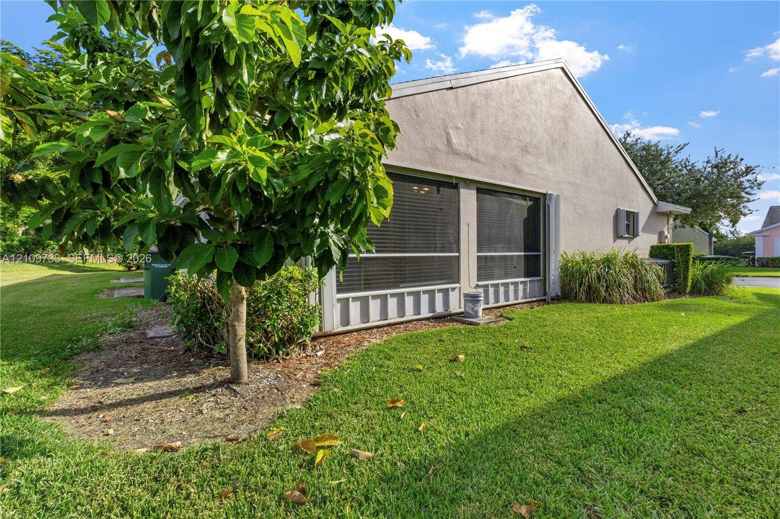 Stucco exterior featuring a screened-in patio, concrete-tile roofing, and established landscaping