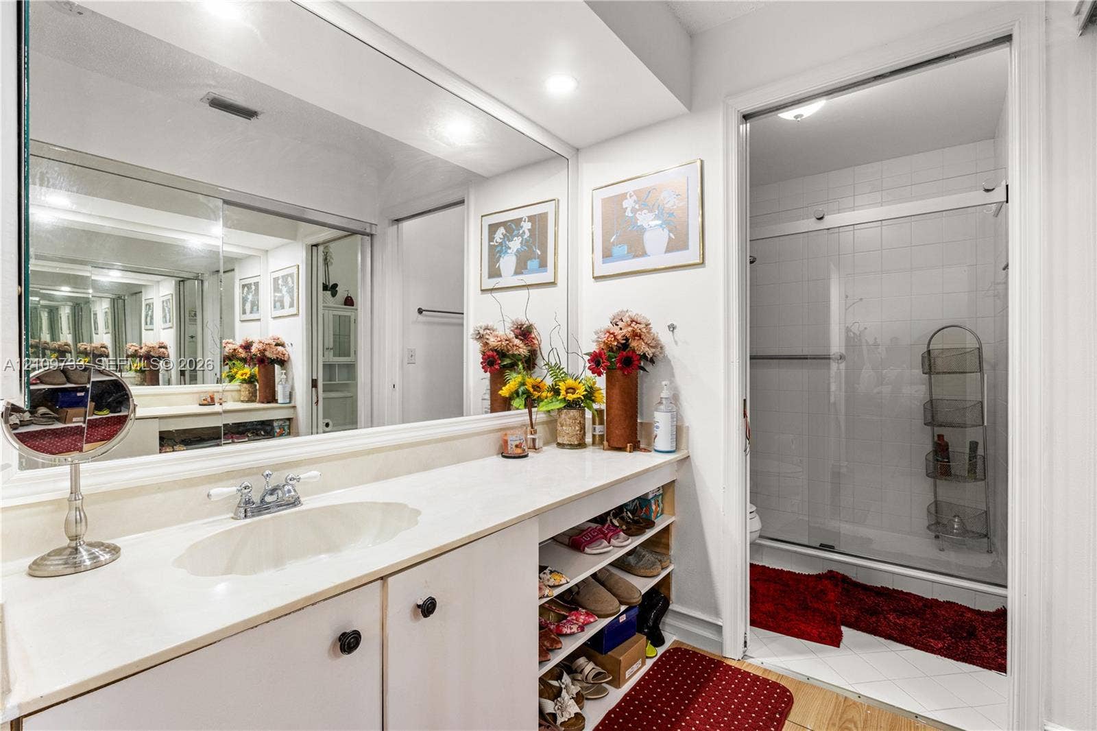 Bathroom featuring a full-width wall mirror, white vanity cabinet with a solid surface countertop, integrated sink, and an enclosed shower with sliding glass doors