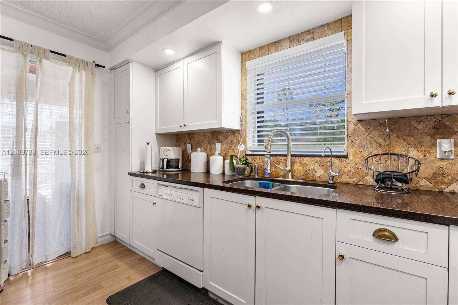 Kitchen featuring white shaker-style cabinetry, dark stone-finish countertops, a stone tile backsplash, a double-basin stainless steel sink with a high-arch faucet, and wood-finish flooring
