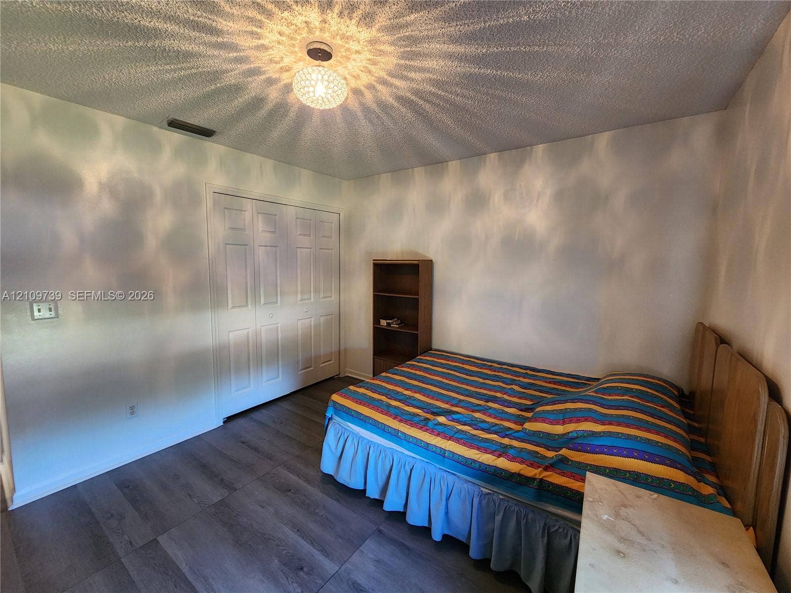 Wood-finish flooring, textured ceiling, and a multi-panel closet door