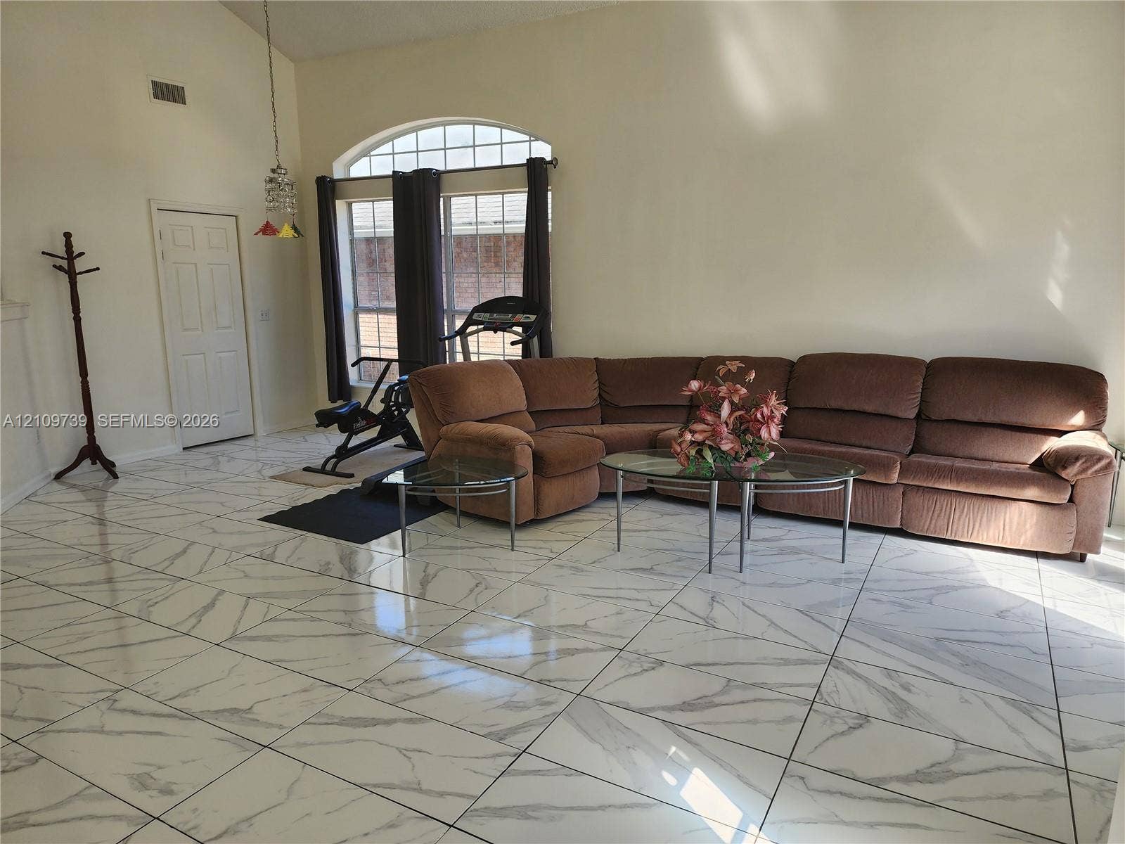 High-ceilinged living area featuring large-format tile flooring with a marble-patterned finish and a prominent arched window