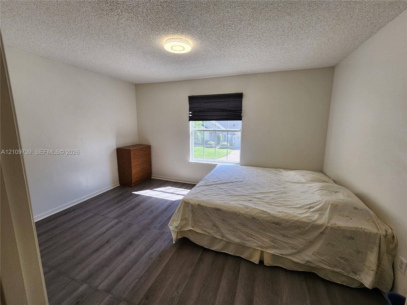 Room featuring wood-finish flooring, a single window, and a central flush-mount ceiling light fixture