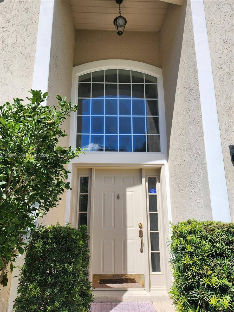 Stucco entryway featuring a paneled door, sidelights, an arched transom window, and a hanging pendant fixture