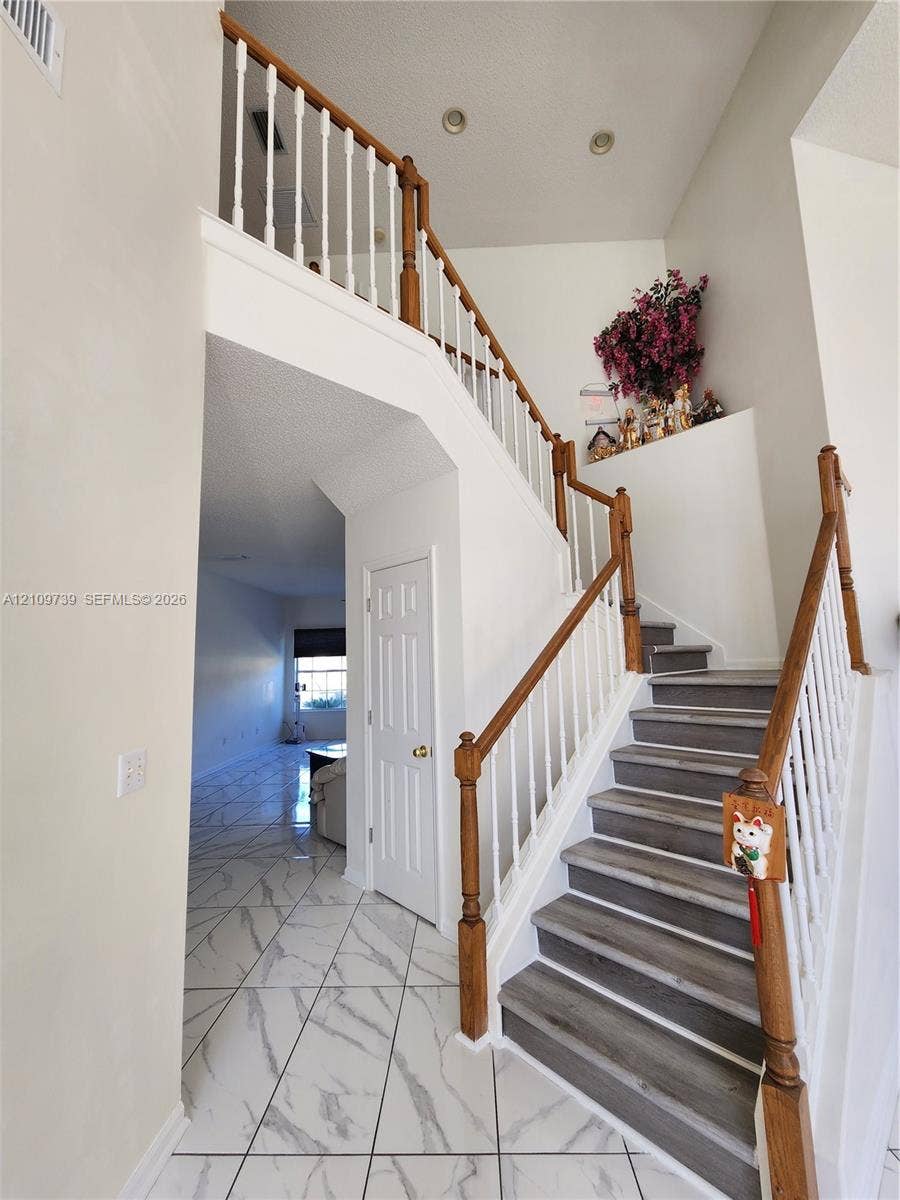 Foyer featuring high ceilings, white tile flooring with gray veining, and a staircase with wood-finish treads and white balusters
