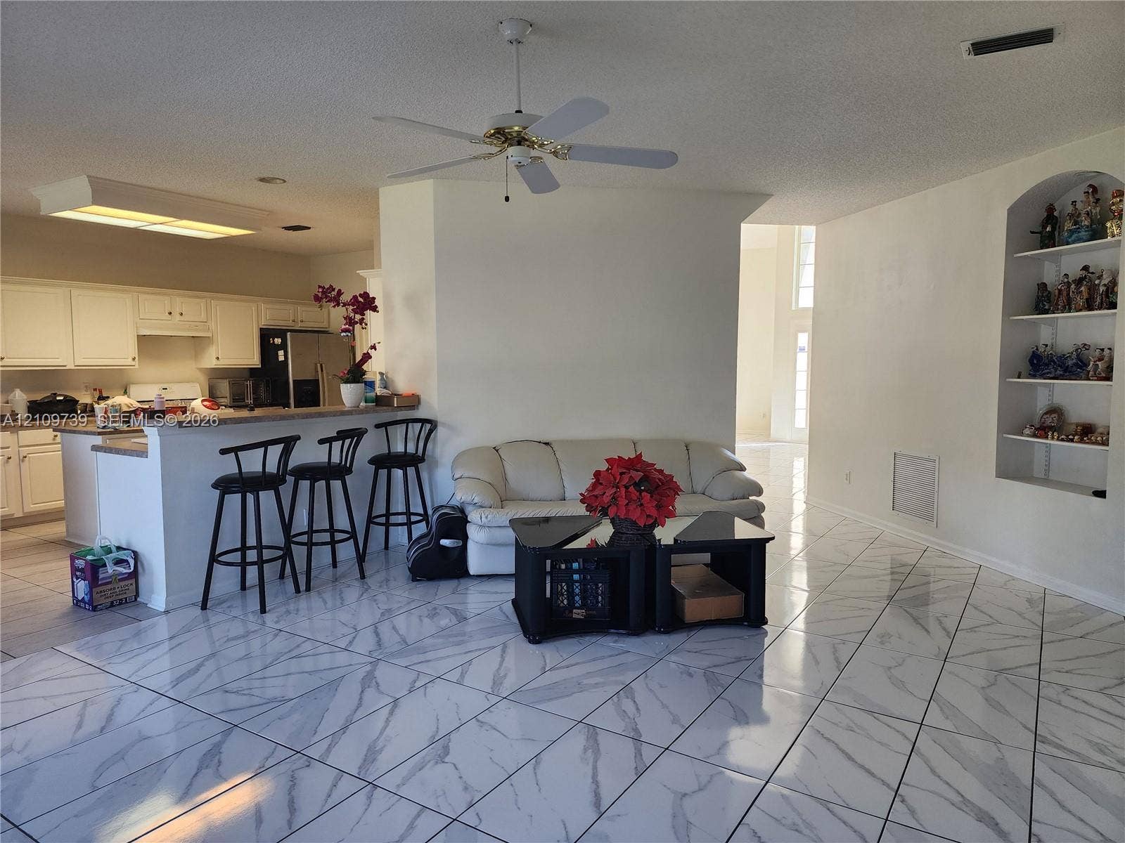 Open-concept interior featuring large-format tile flooring with marble-patterned veining, white cabinetry, a built-in arched display niche, and a ceiling fan with light fixture