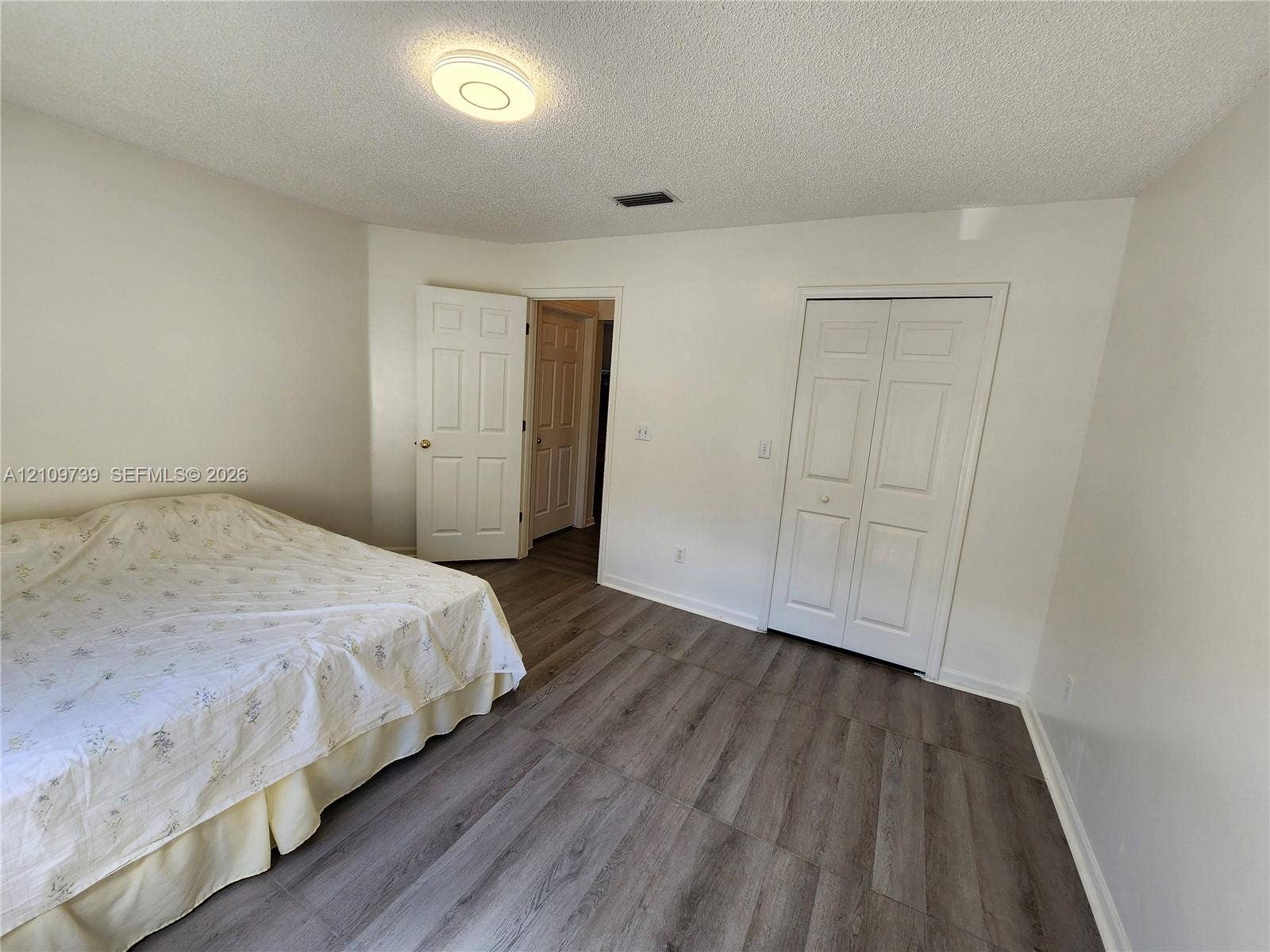 Wood-finish flooring, two-panel interior doors, and a double-door closet with a flush-mount circular ceiling fixture