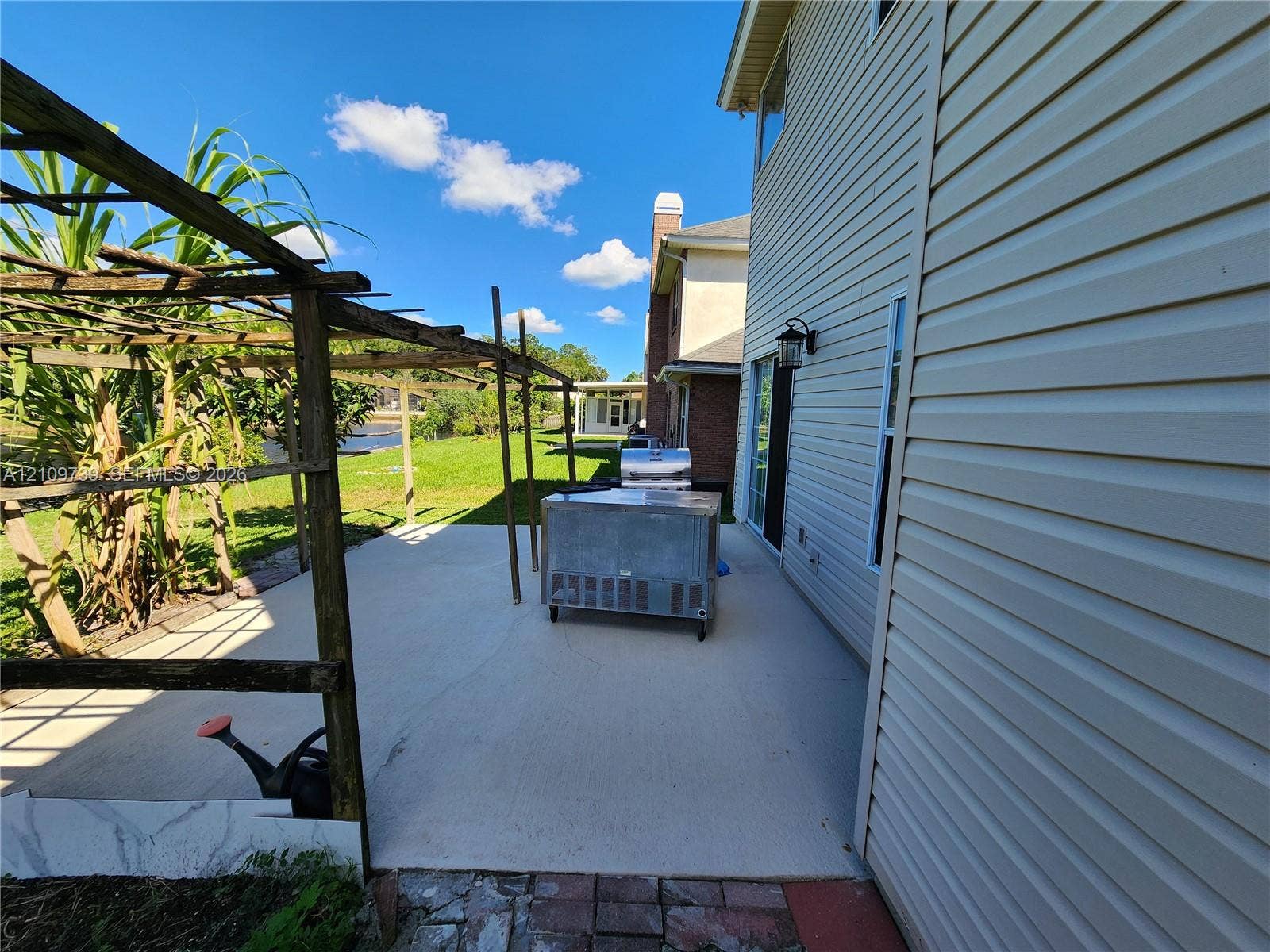 Concrete patio featuring a wood-frame trellis, exterior wall-mounted lighting, and a stainless steel built-in grill