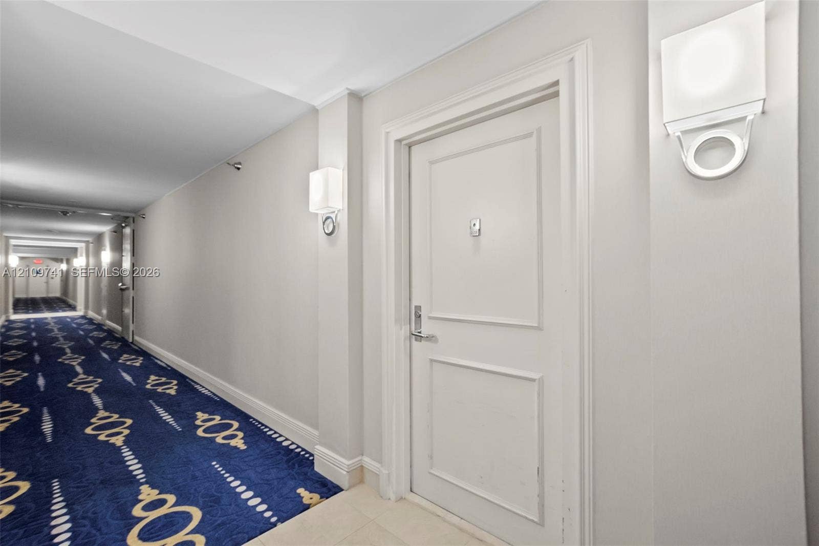 19101 NE 36th Court, #203, Aventura, FL 33180 Hallway featuring patterned carpet flooring, white paneled interior doors, and modern wall-mounted light fixtures
