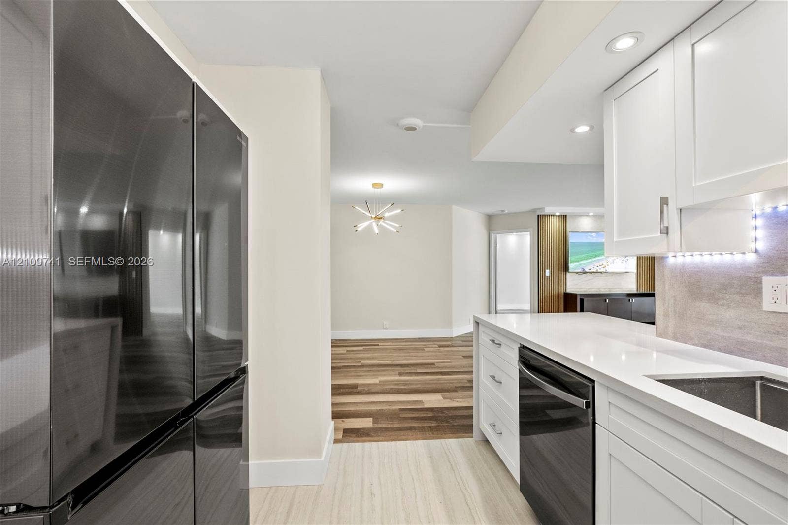19101 NE 36th Court, #203, Aventura, FL 33180 Kitchen featuring white shaker-style cabinetry, quartz countertops, integrated under-cabinet lighting, a stainless steel dishwasher, and a full-size dark-finish refrigerator
