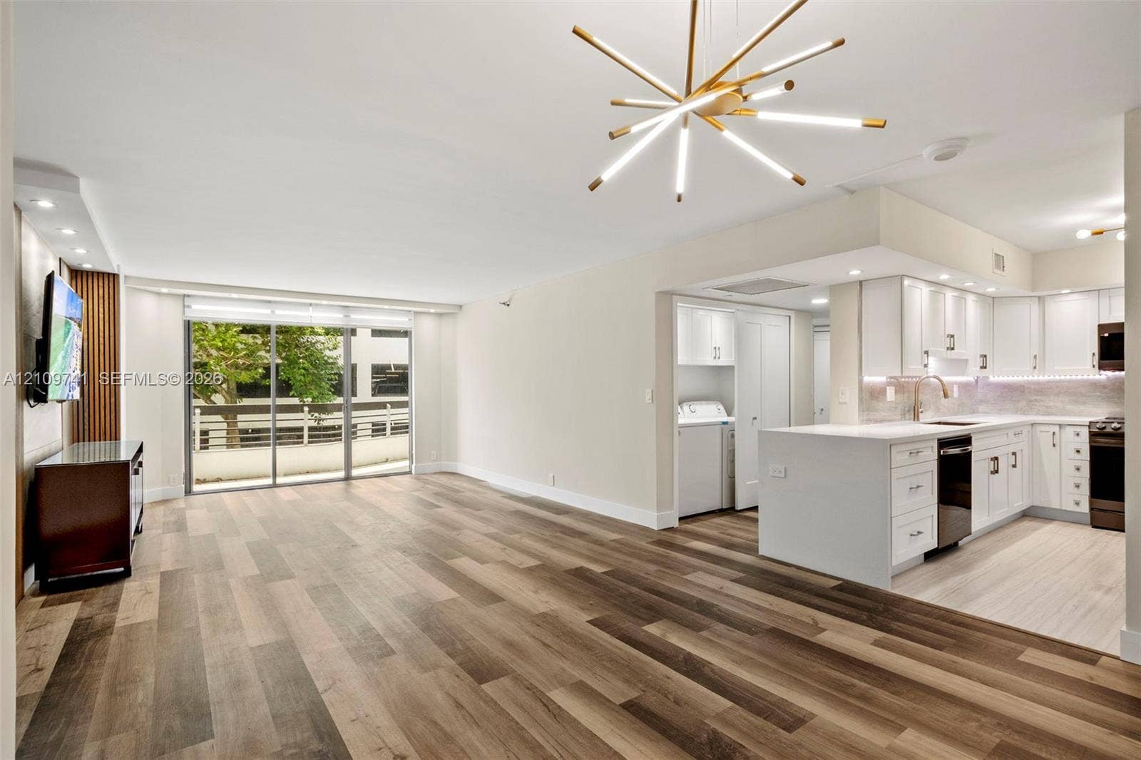 19101 NE 36th Court, #203, Aventura, FL 33180 Open-concept area featuring wood-finish flooring, a modern sputnik-style chandelier, and floor-to-ceiling sliding glass doors